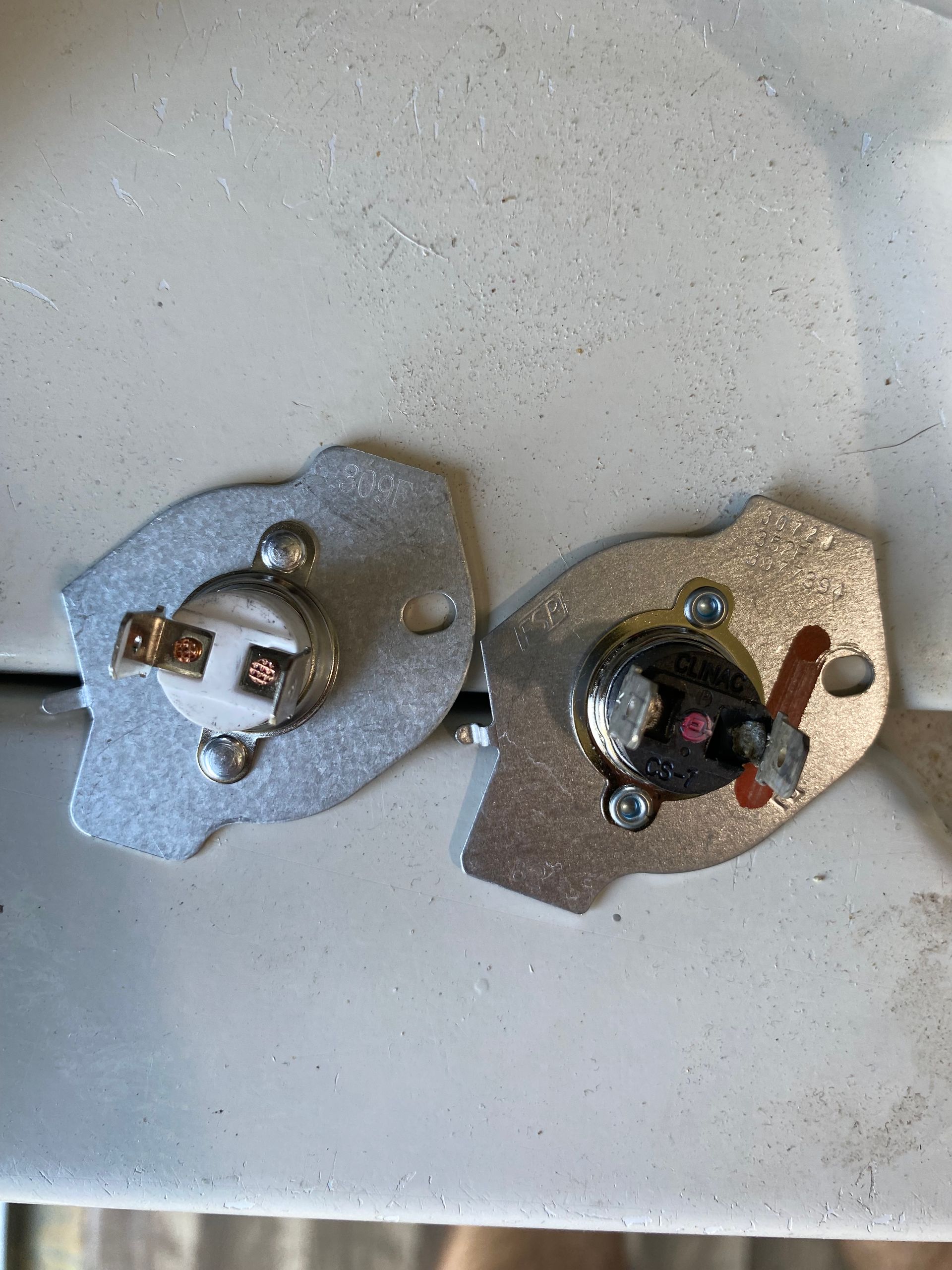 Two thermostats on metal plates. One with tan, one with black sensor, with electrical contacts.