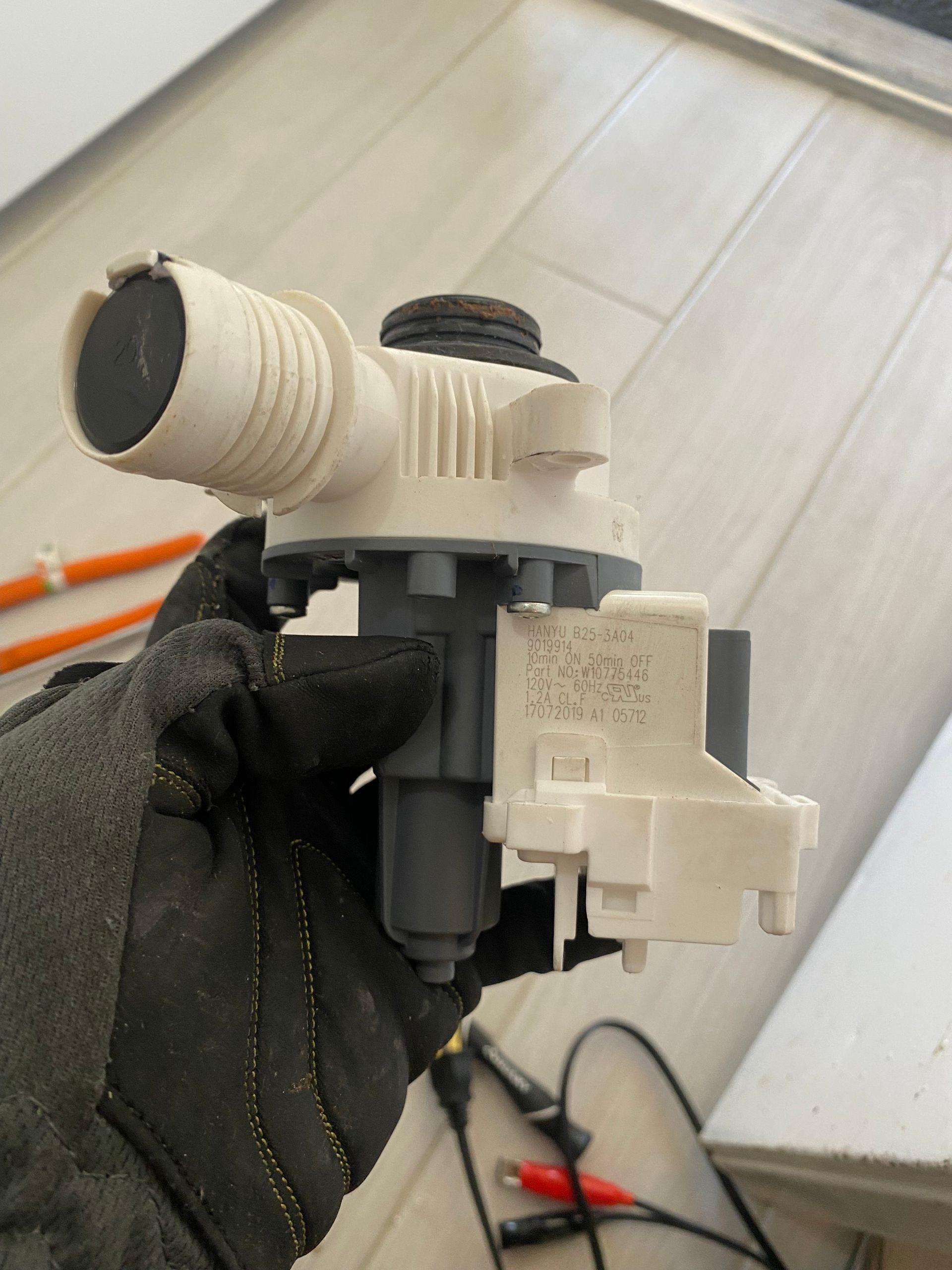 A person in a black glove holds a white and gray appliance pump against a light-colored surface.