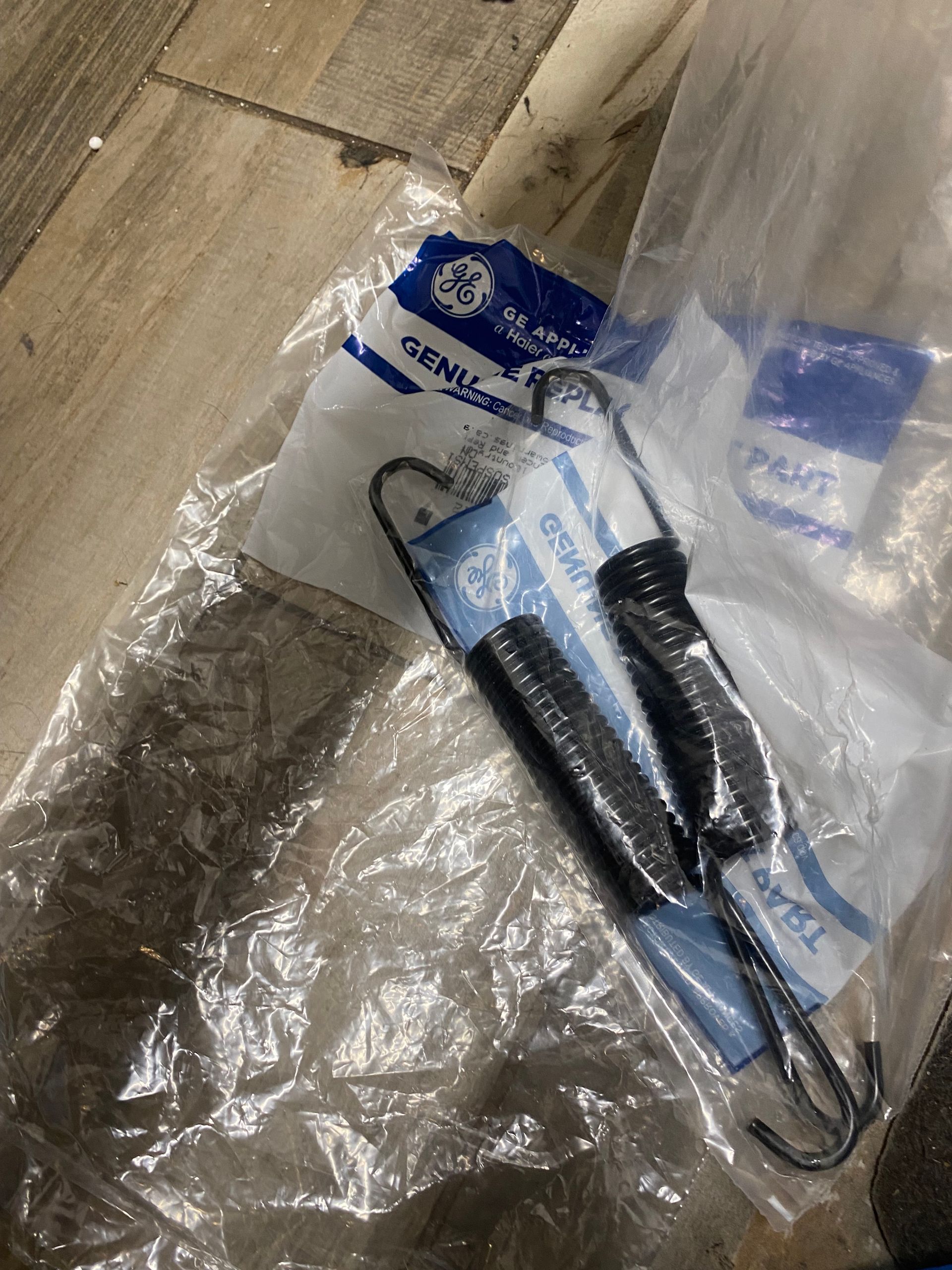 Two black coil springs with hooks in a GE-branded plastic bag.