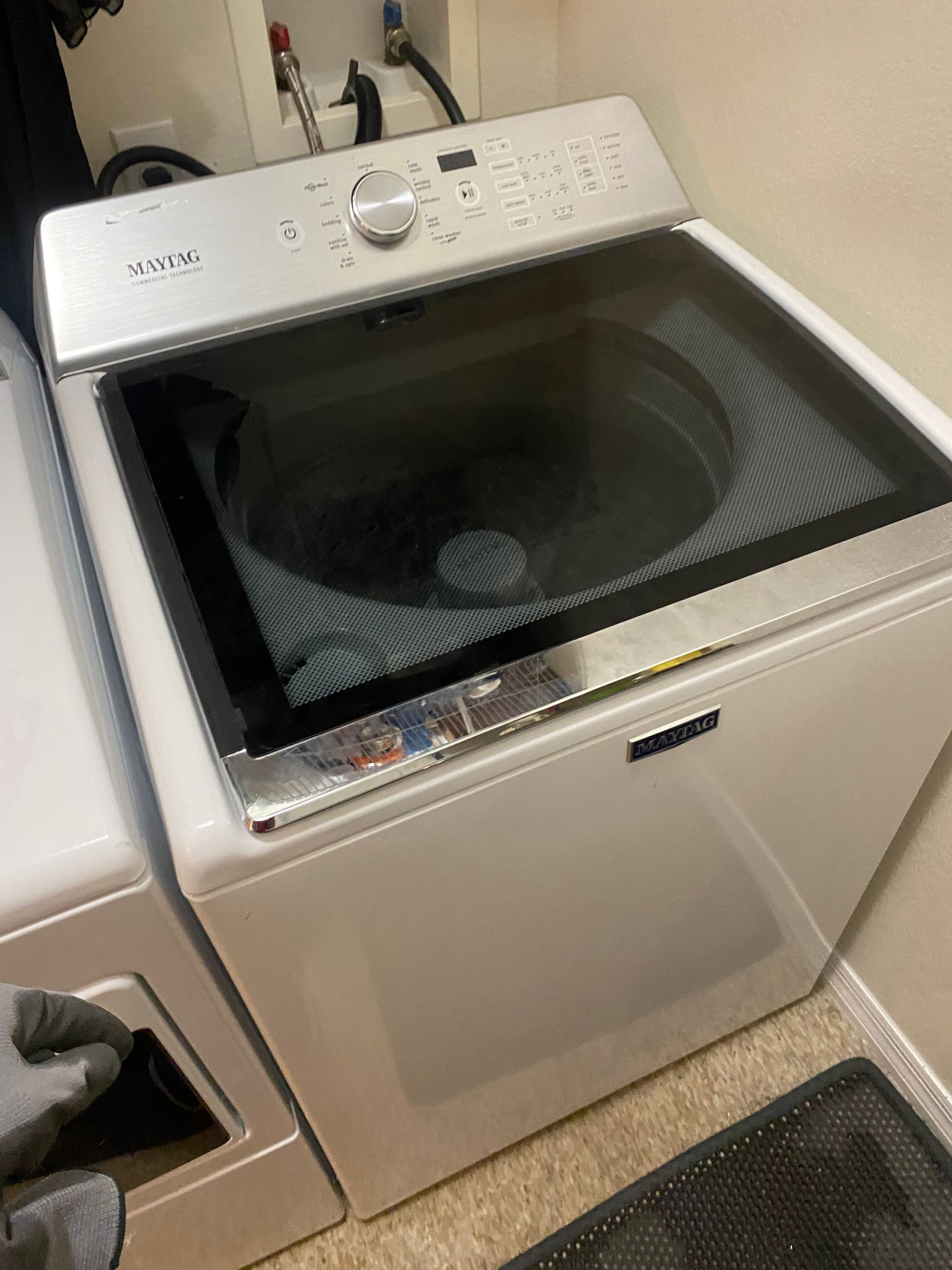 White Samsung top-load washing machine with glass lid in a laundry room.