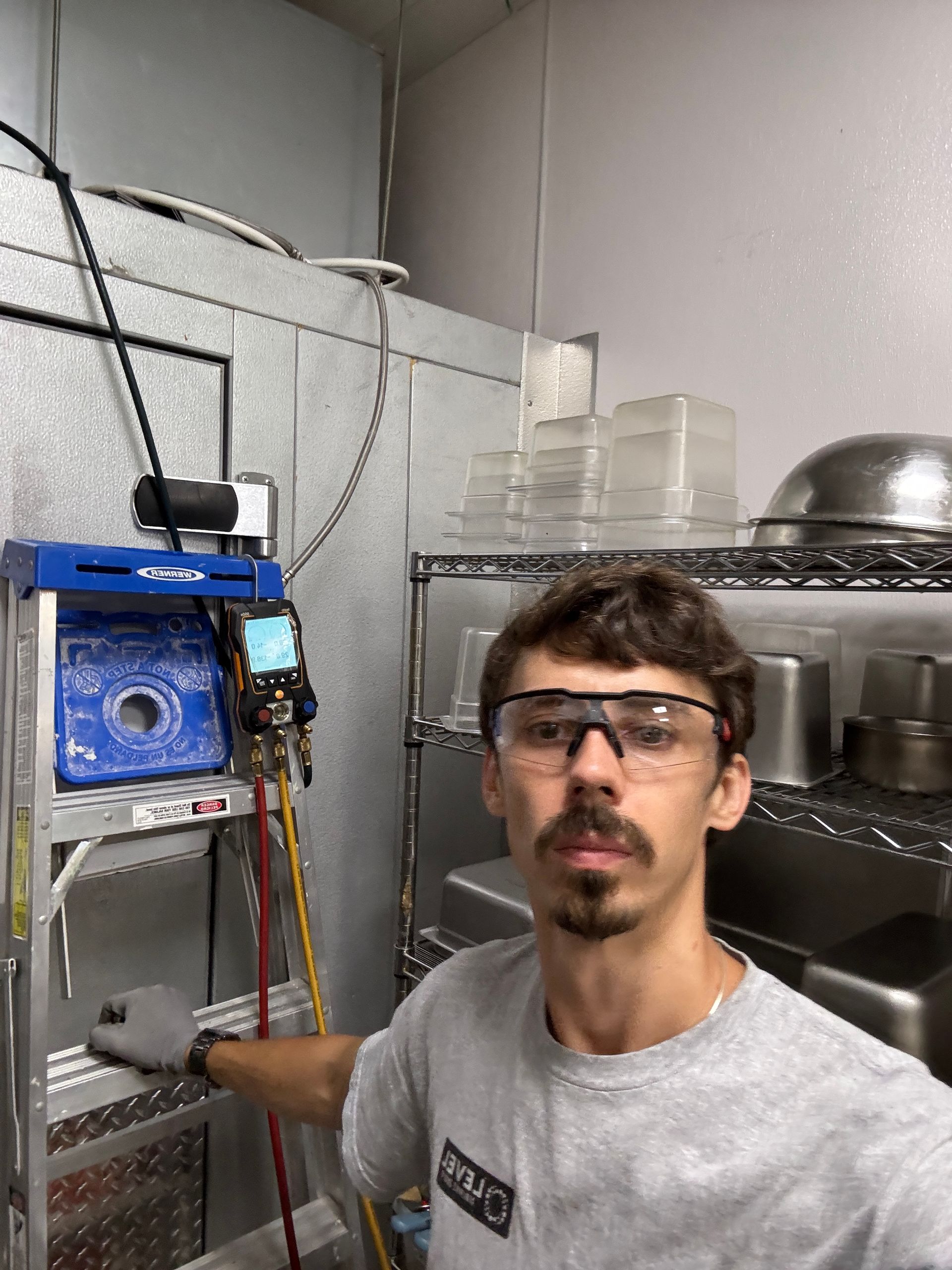 Person with safety glasses working on refrigeration unit in a commercial kitchen.