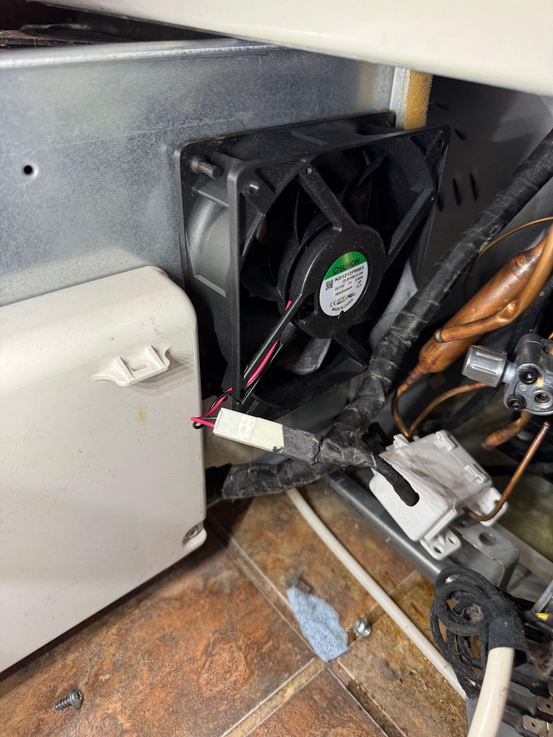Black fan in a refrigerator. Wires and components are visible. Beige and silver interior.