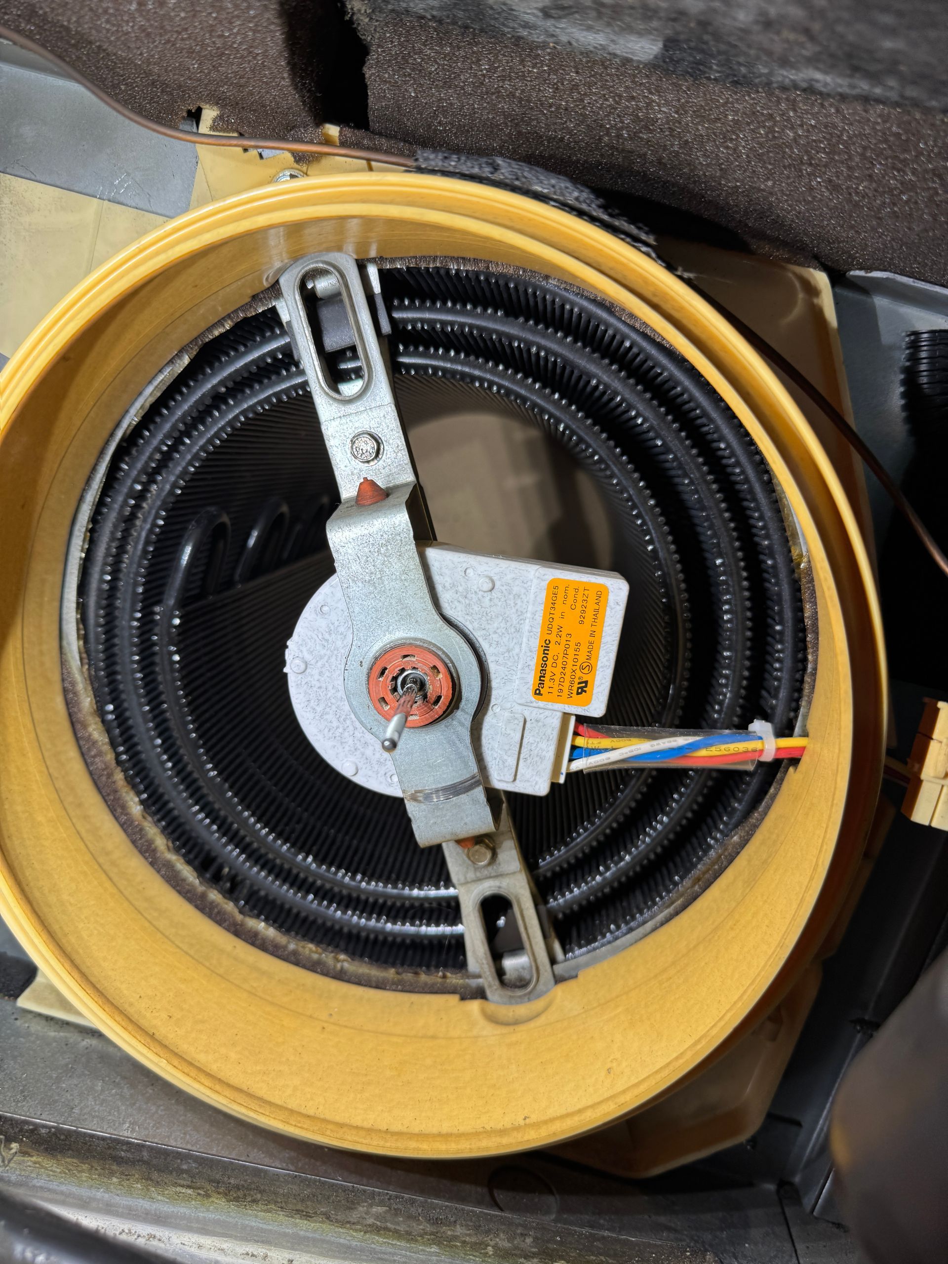 Circular yellow container holding coiled black tube with a metal mechanism; colorful wires attached.