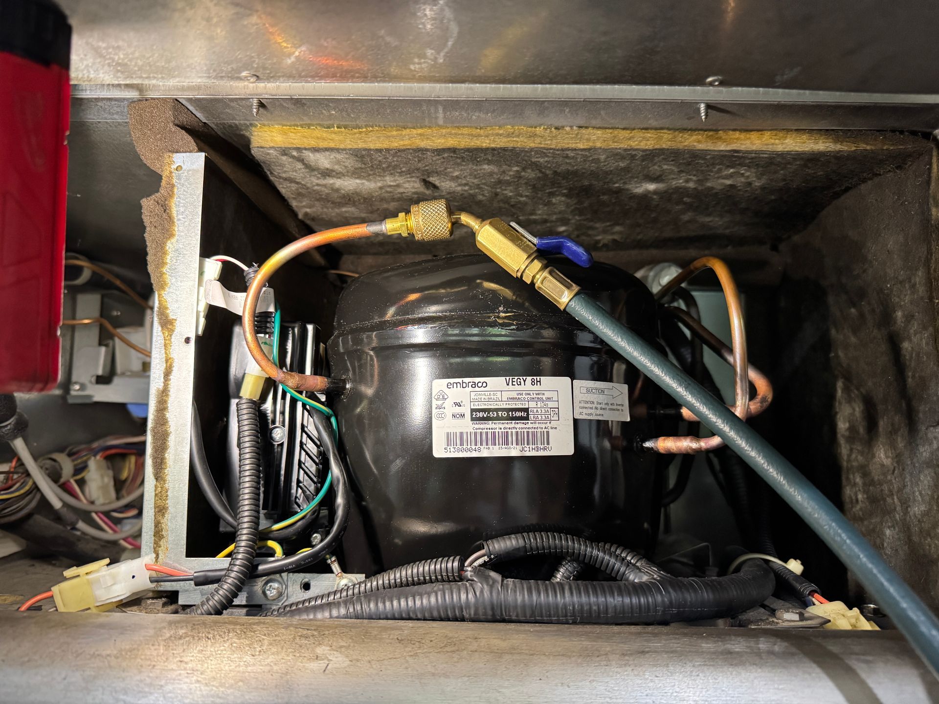 Refrigerator compressor with connected copper and black hoses, wires, and insulation.