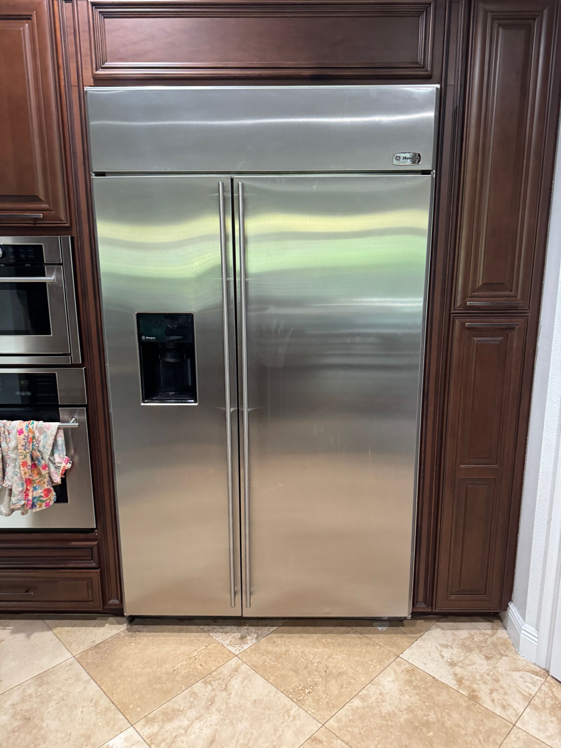 Stainless steel refrigerator built into dark wood cabinets in a kitchen setting.