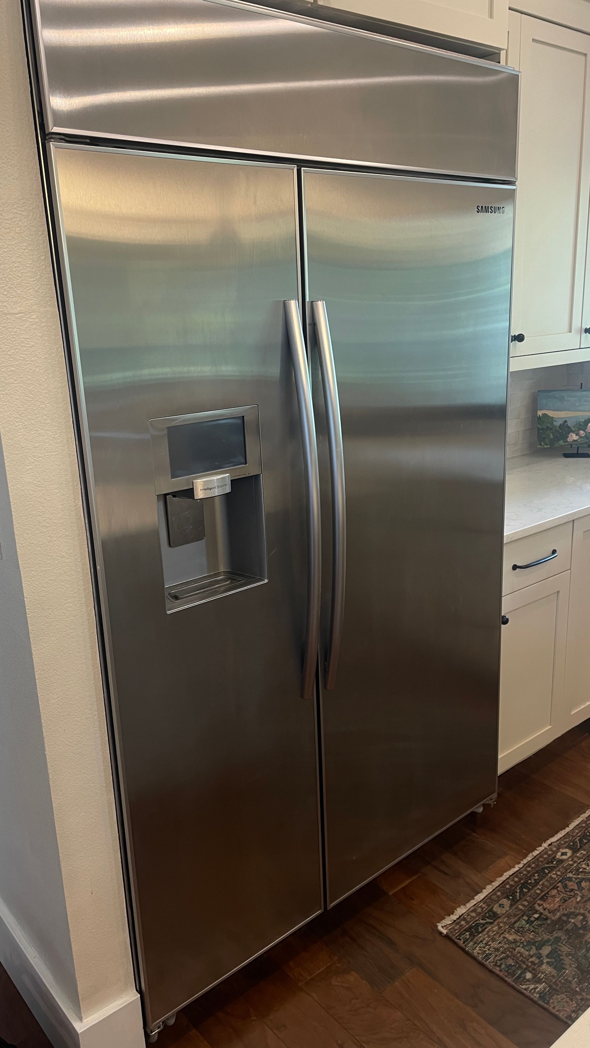 Stainless steel side-by-side refrigerator in a kitchen setting; the left door has an ice/water dispenser.