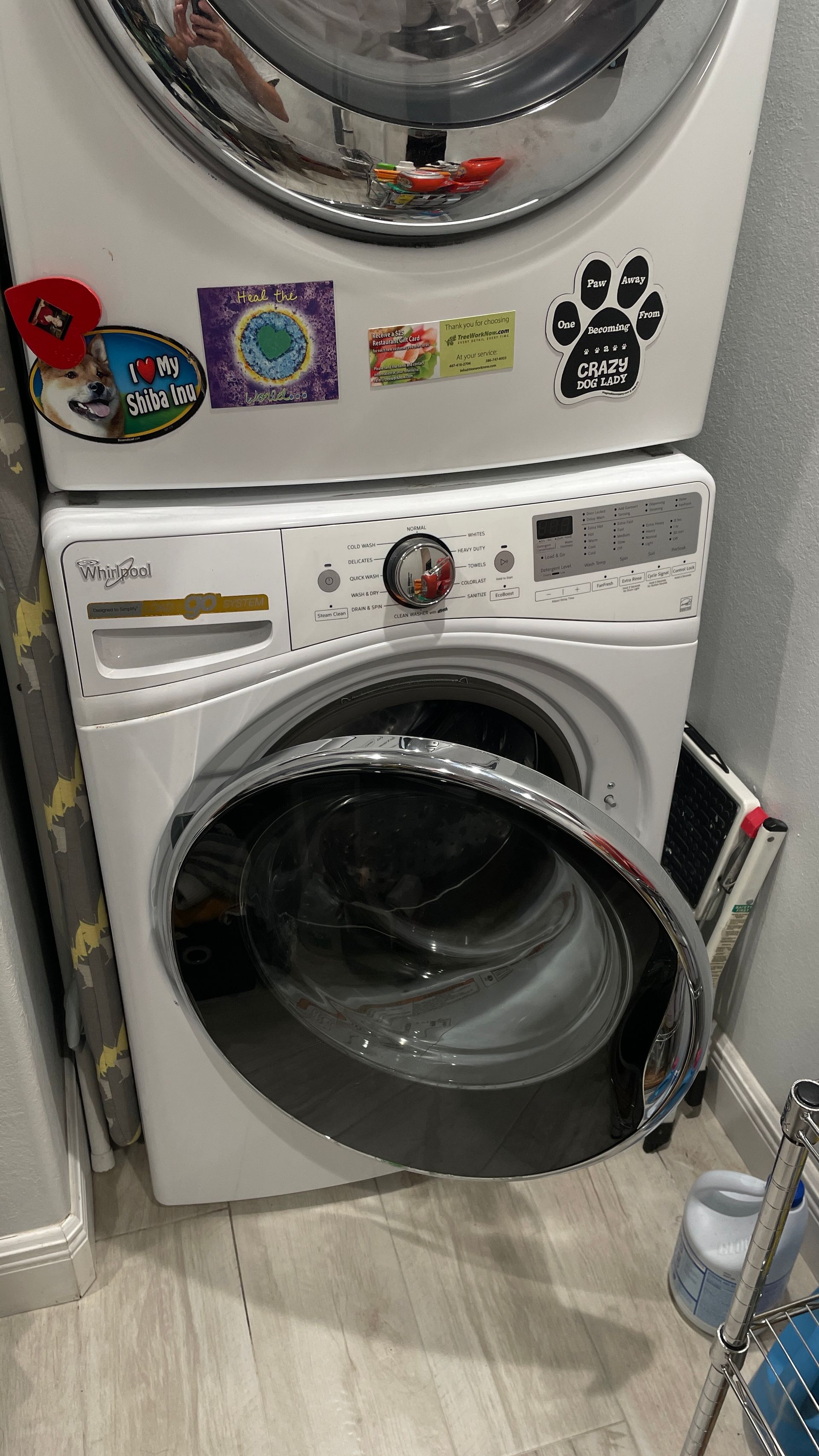 White stacked Whirlpool washer and dryer, the washer door open, on a wood floor.