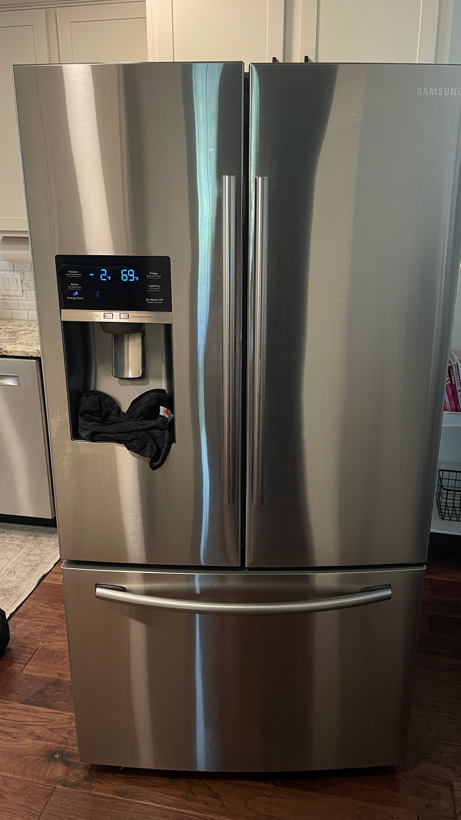 Stainless steel French door refrigerator with water dispenser in a kitchen.