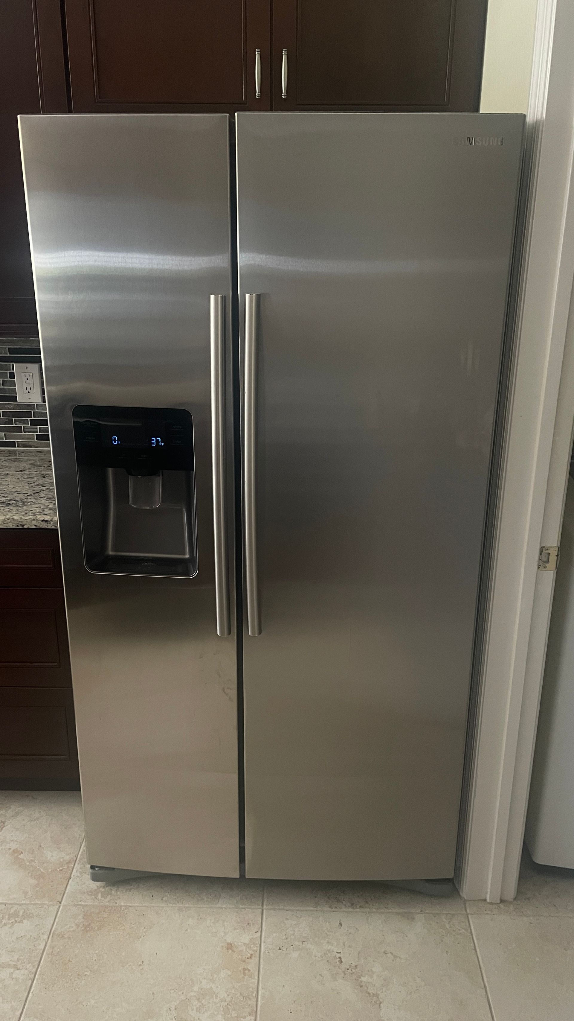 Stainless steel side-by-side refrigerator in a kitchen with a water dispenser on the left door.