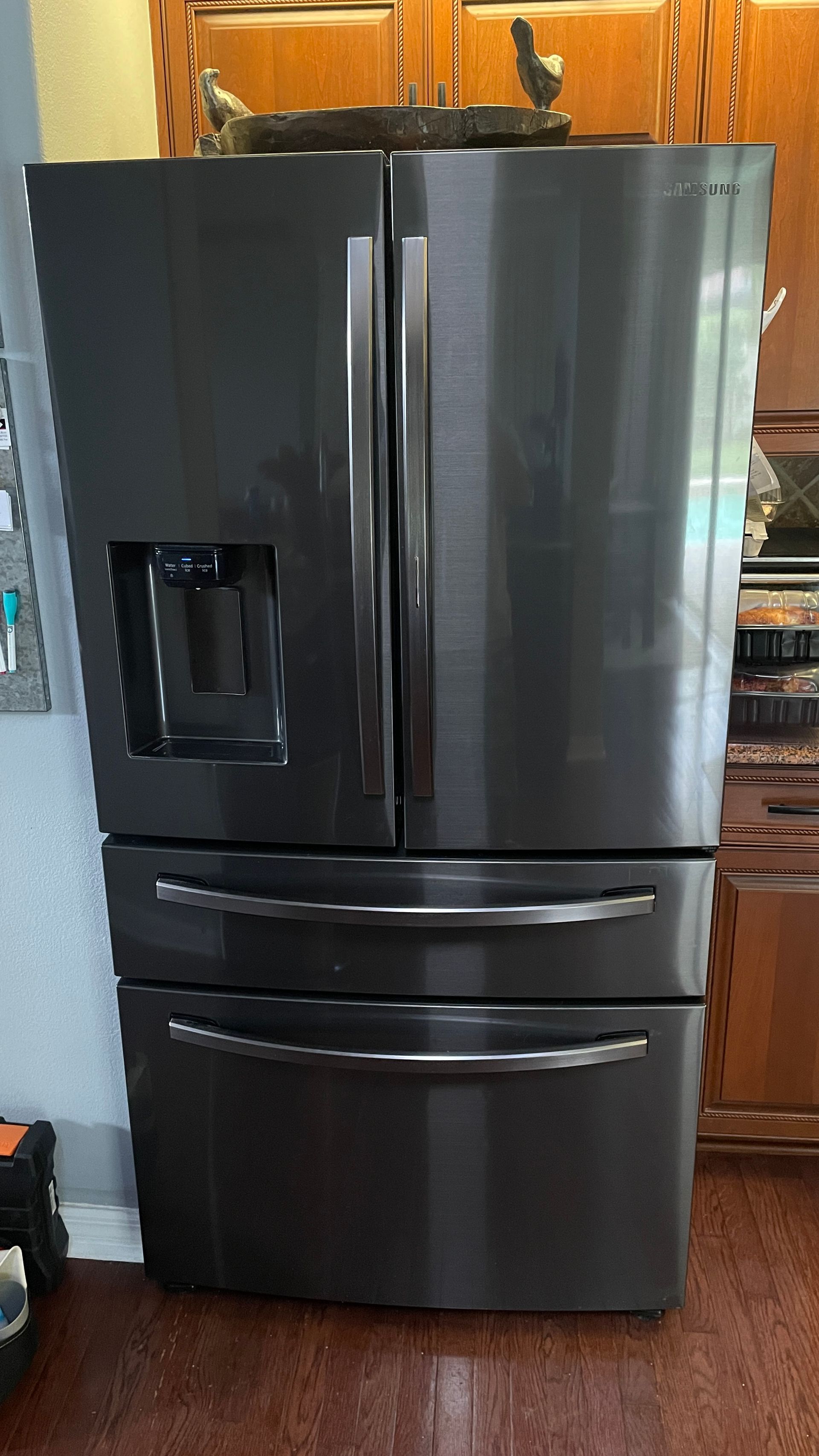 Black stainless steel French door refrigerator with water dispenser in a kitchen.