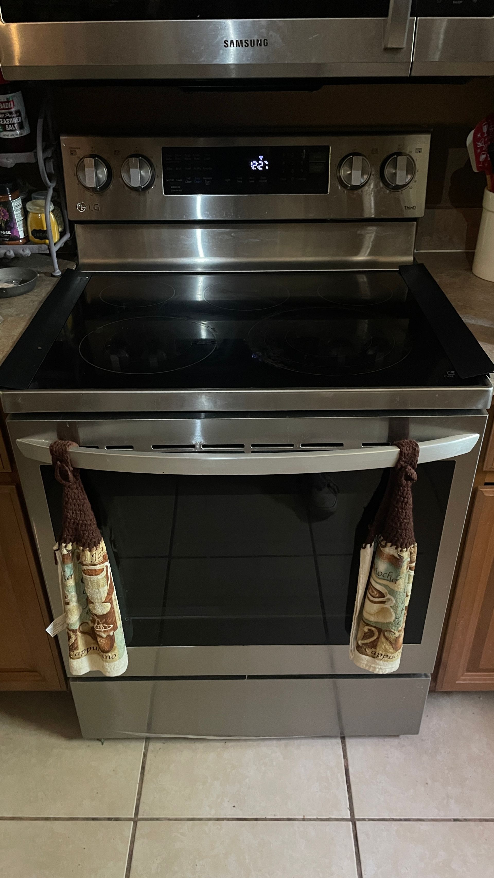 Stainless steel electric range with black cooktop, oven door, and two kitchen towels hanging from the handle.