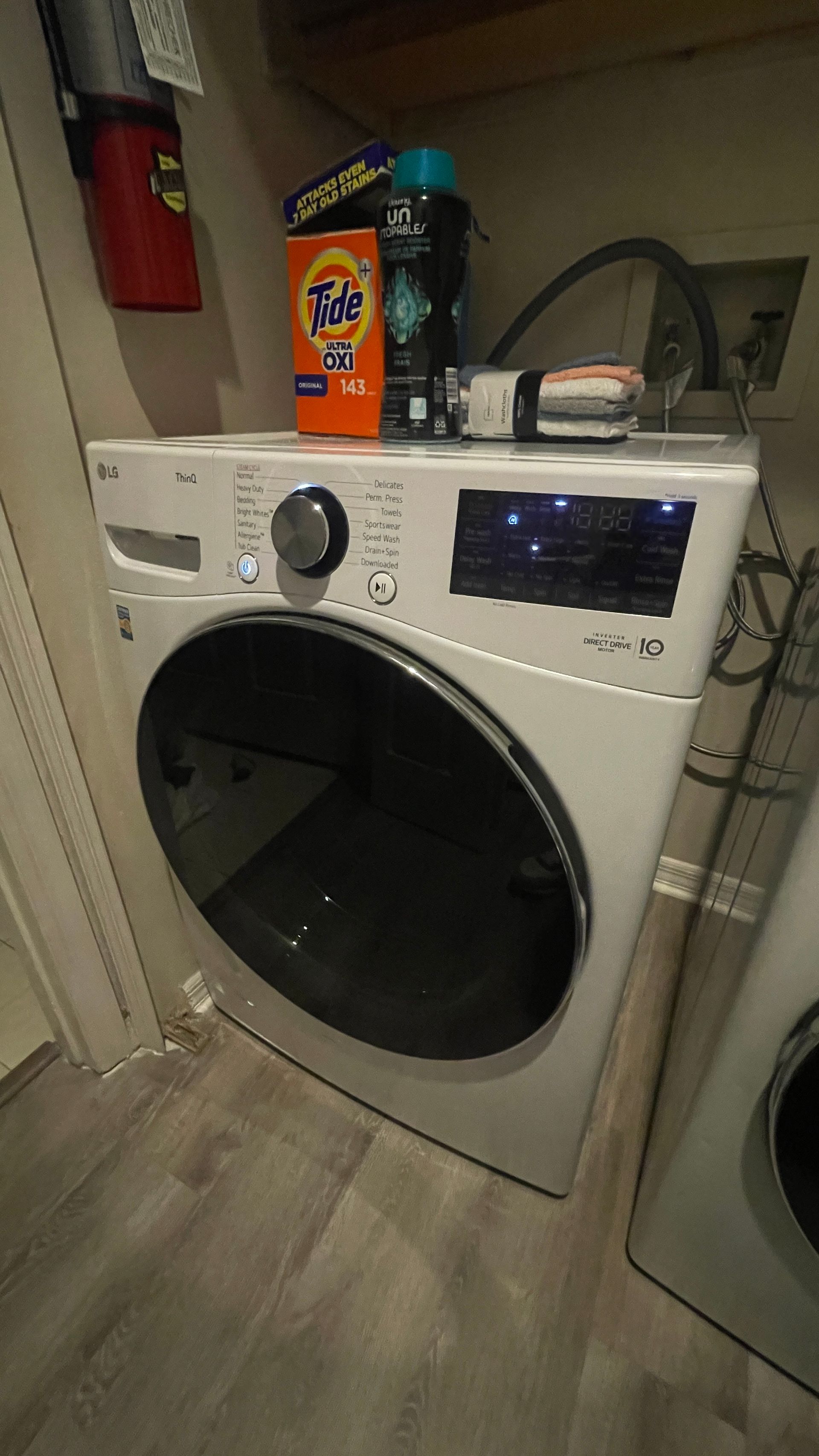 White LG washing machine with Tide detergent and other items on top in a laundry room.
