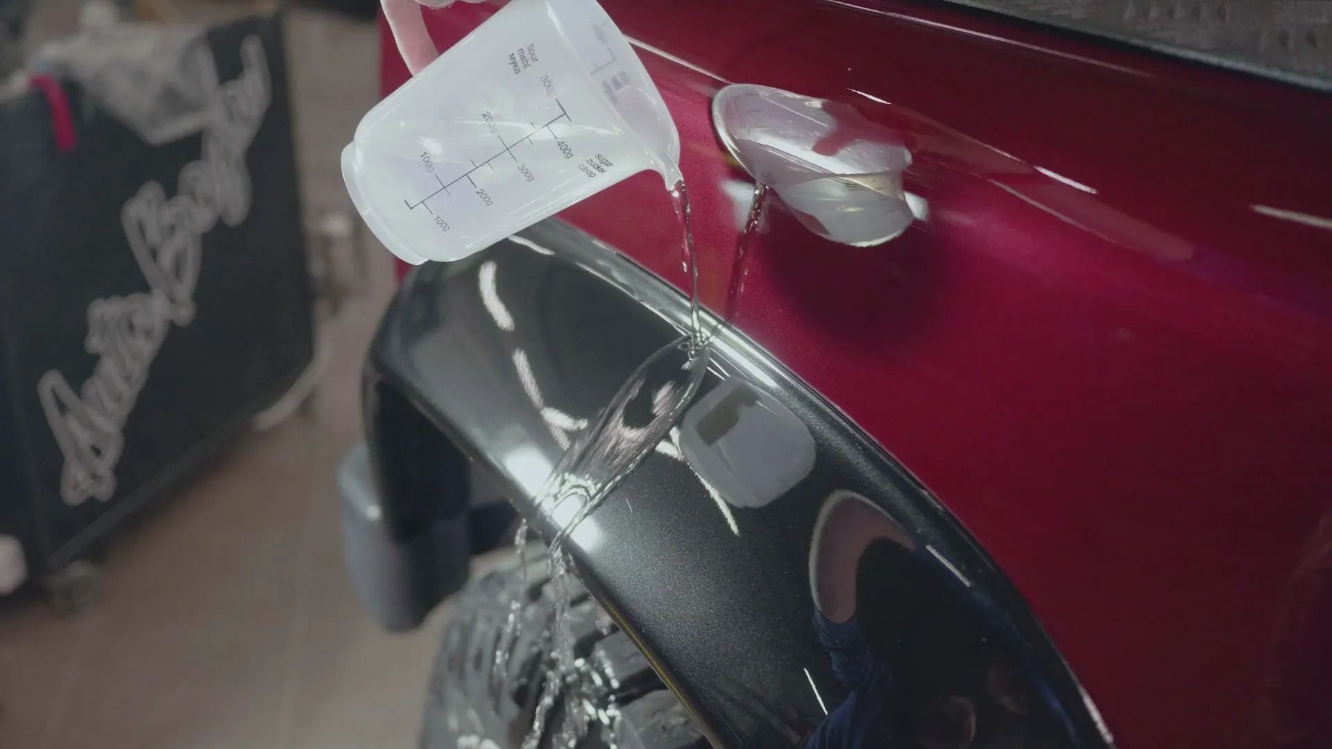 Close-up of a red car’s side panel with a dangling white tag and black wheel arch mirror-like trim.