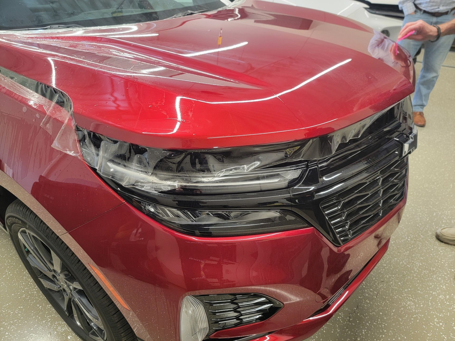 Damaged red SUV front end with crumpled hood and broken grille in a repair shop