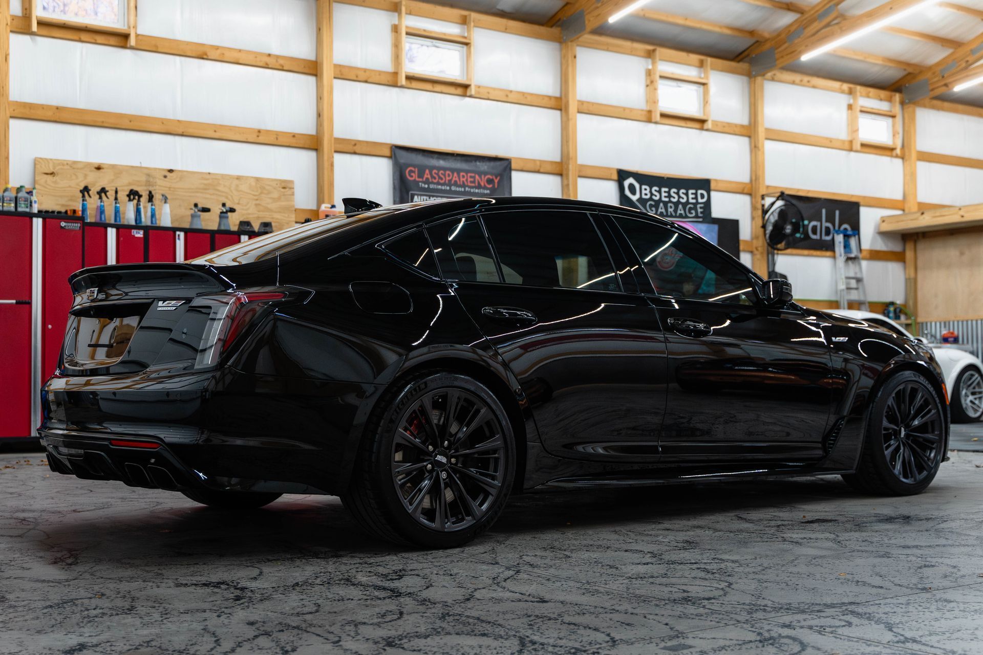Black sports sedan in a garage workshop, viewed from the side with glossy paint and tinted windows