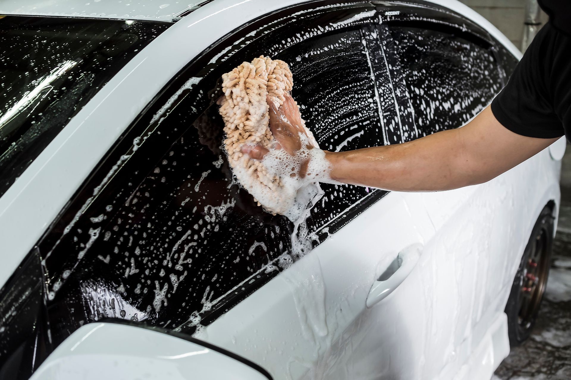 Person washing a white car window with soapy sponge in a car wash