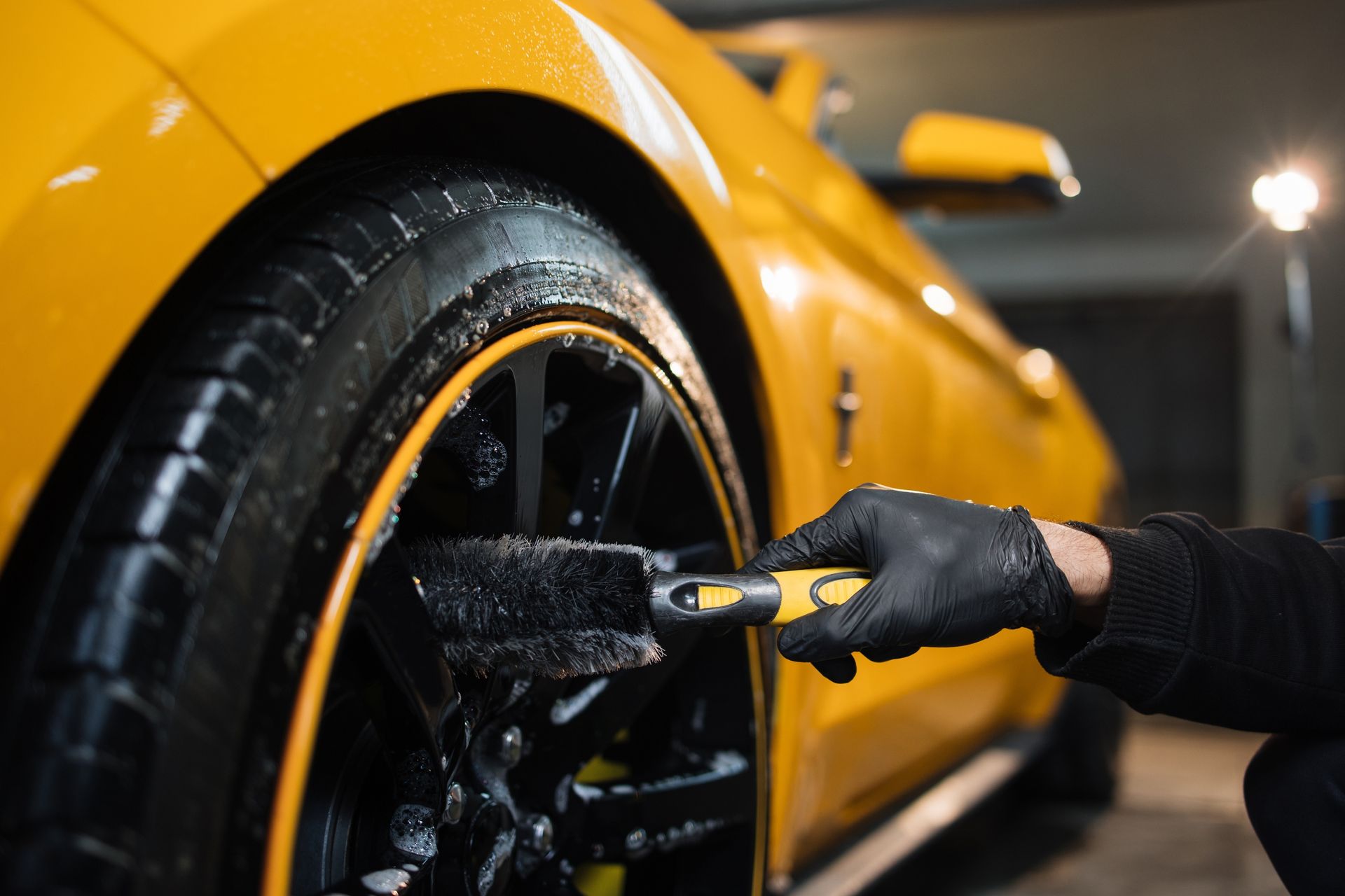 Hand washing the wheel of a yellow car with a brush in a dark garage