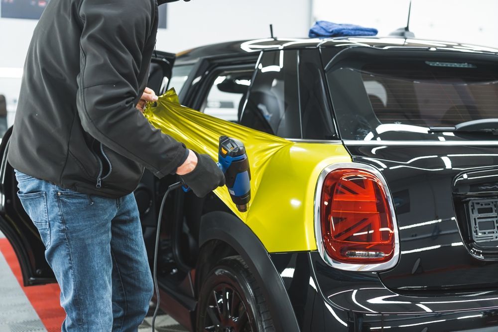 Person wraps yellow vinyl on a black car at an auto shop