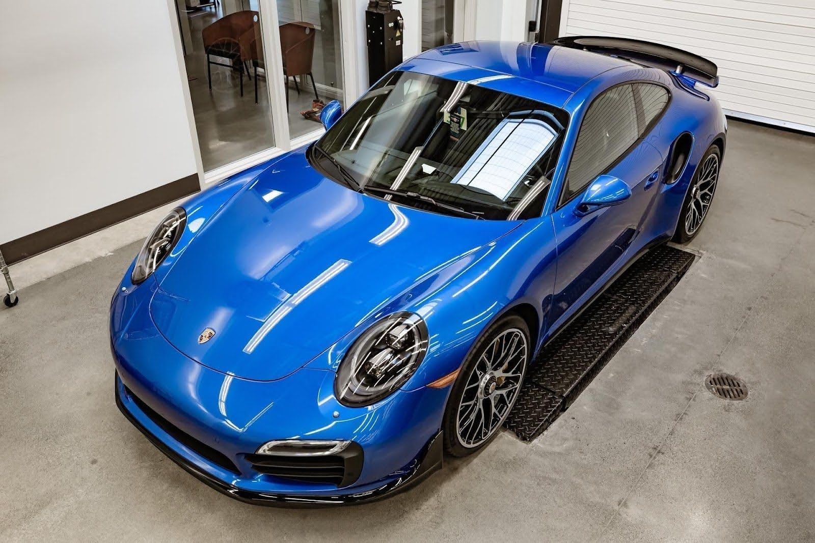 Blue sports car parked indoors on a concrete floor, viewed from above.