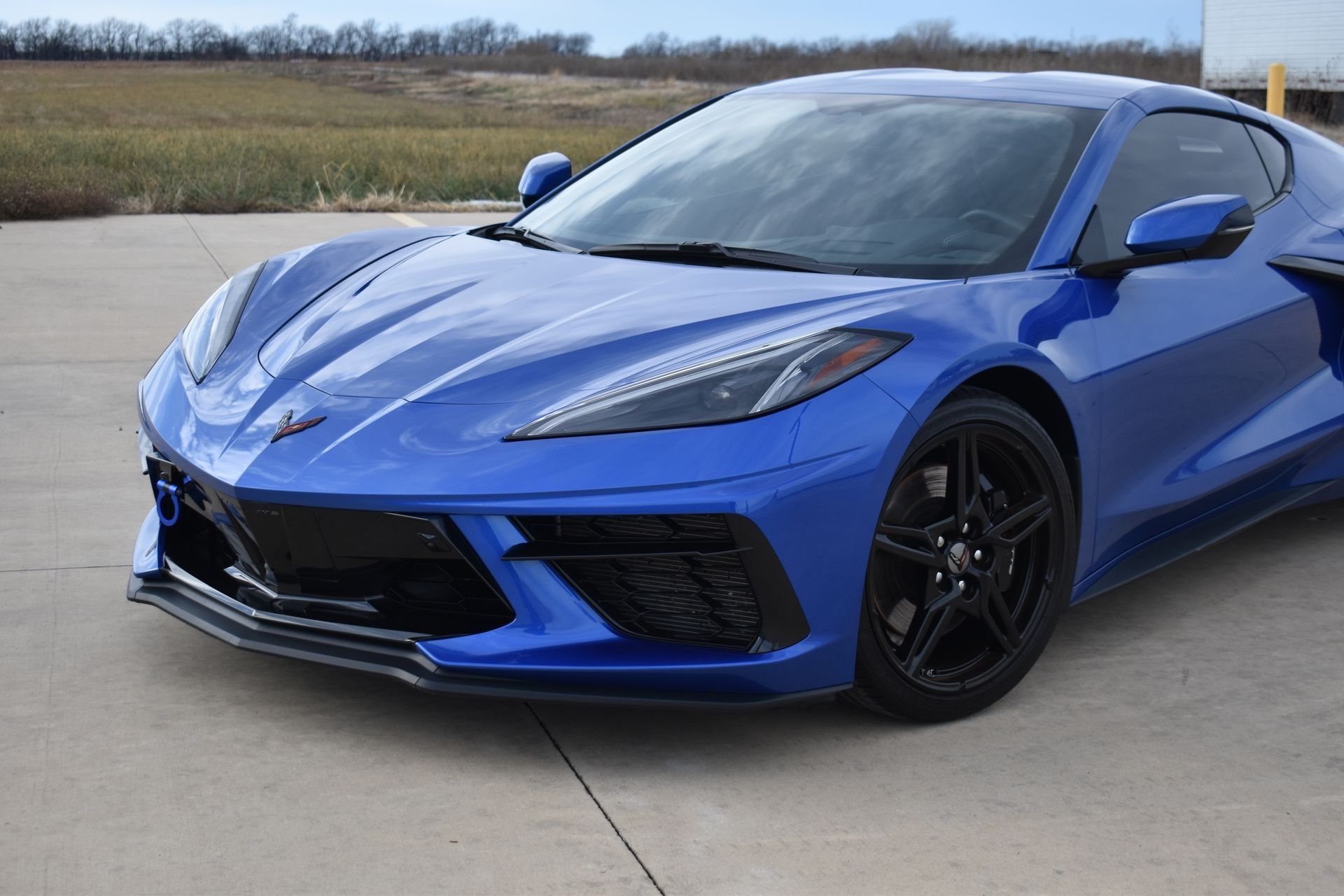 Blue sports car parked on a concrete lot with fields in the background