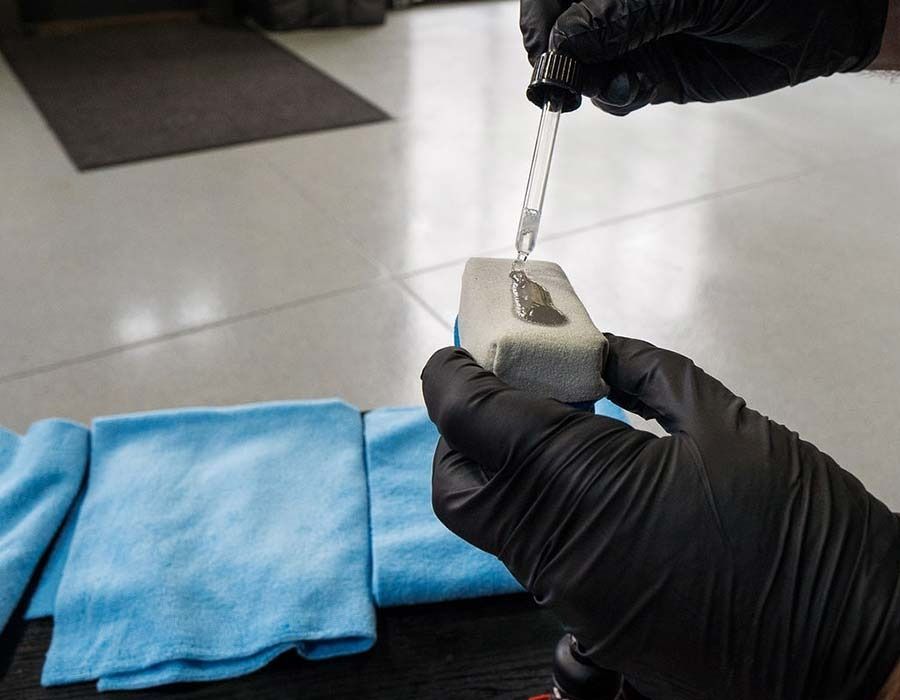 Gloved hands handling a small key over a gray lock on a table with a blue cloth