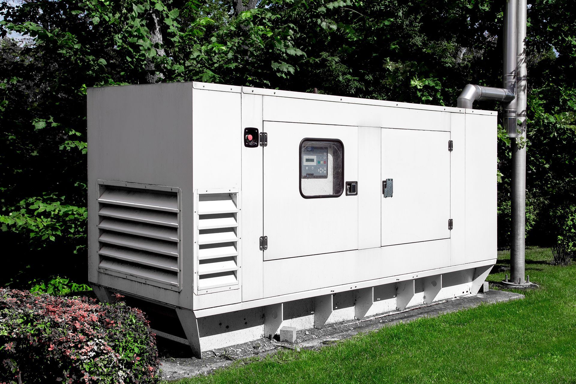 Large white generator unit outdoors on a concrete pad beside grass and trees