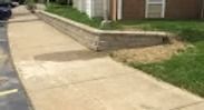 Sidewalk beside a building with a low stone retaining wall and grass lawn