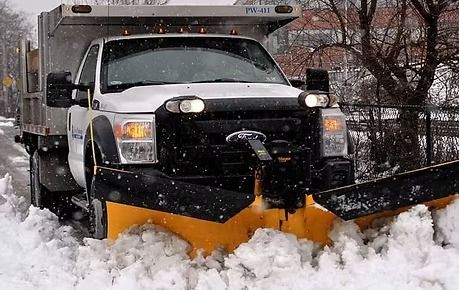 Snowplow truck clearing deep snow on a city street during snowfall