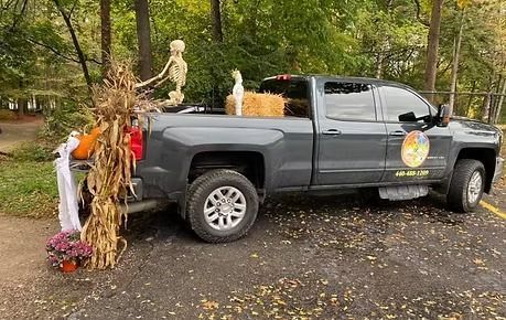Black pickup truck decorated for Halloween with hay bales and pumpkins in a wooded driveway