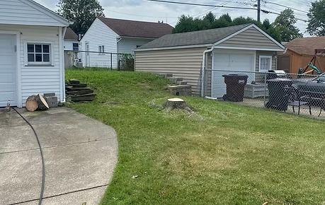 Backyard with concrete driveway, grassy slope, detached garage, and houses in the background