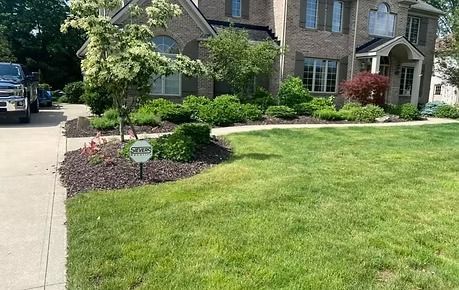 Suburban house with manicured lawn, driveway, and landscaped front garden on a sunny day