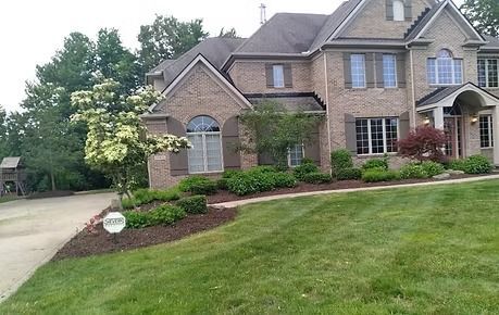 Large brick suburban house with a manicured lawn and driveway on a tree-lined street