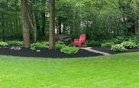 Lush backyard garden with green lawn, dark mulch beds, trees, and a red Adirondack chair near a path