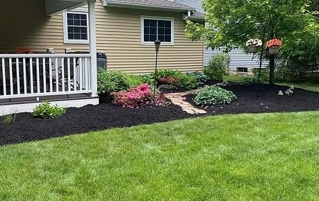 Front yard flower bed with pink and white flowers, dark mulch, and a white porch railing by the house