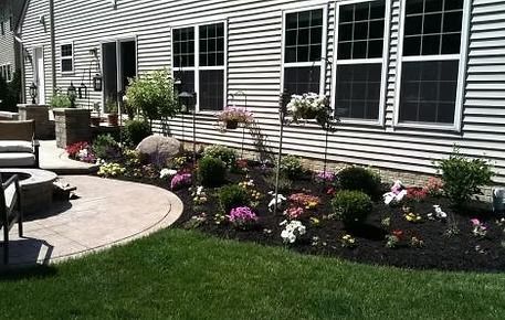 House exterior with a curved flower bed of colorful blooms beside a patio and green lawn