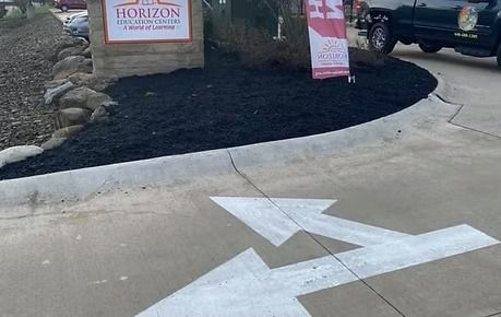 Arrow on concrete driveway pointing left toward a Horizon sign and landscaped entrance.