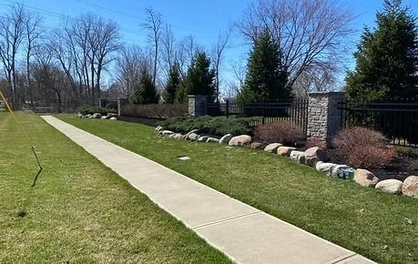 Paved walkway beside a grassy lawn and landscaped stone border under a clear blue sky