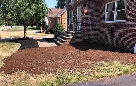 Brick house exterior with front steps and a large mulched yard area near the sidewalk.