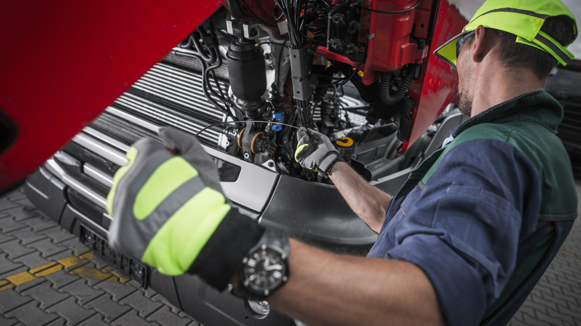 Mechanic working on machinery, wearing gloves and a safety vest, in an industrial setting