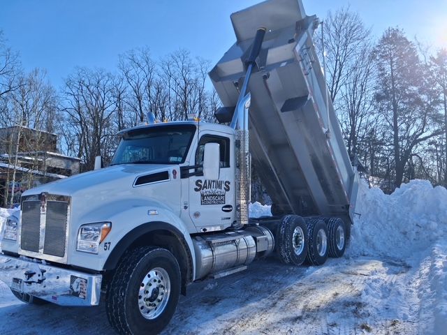 Santini's White dump truck tipping its raised bed to unload snow beside a snowy roadside.