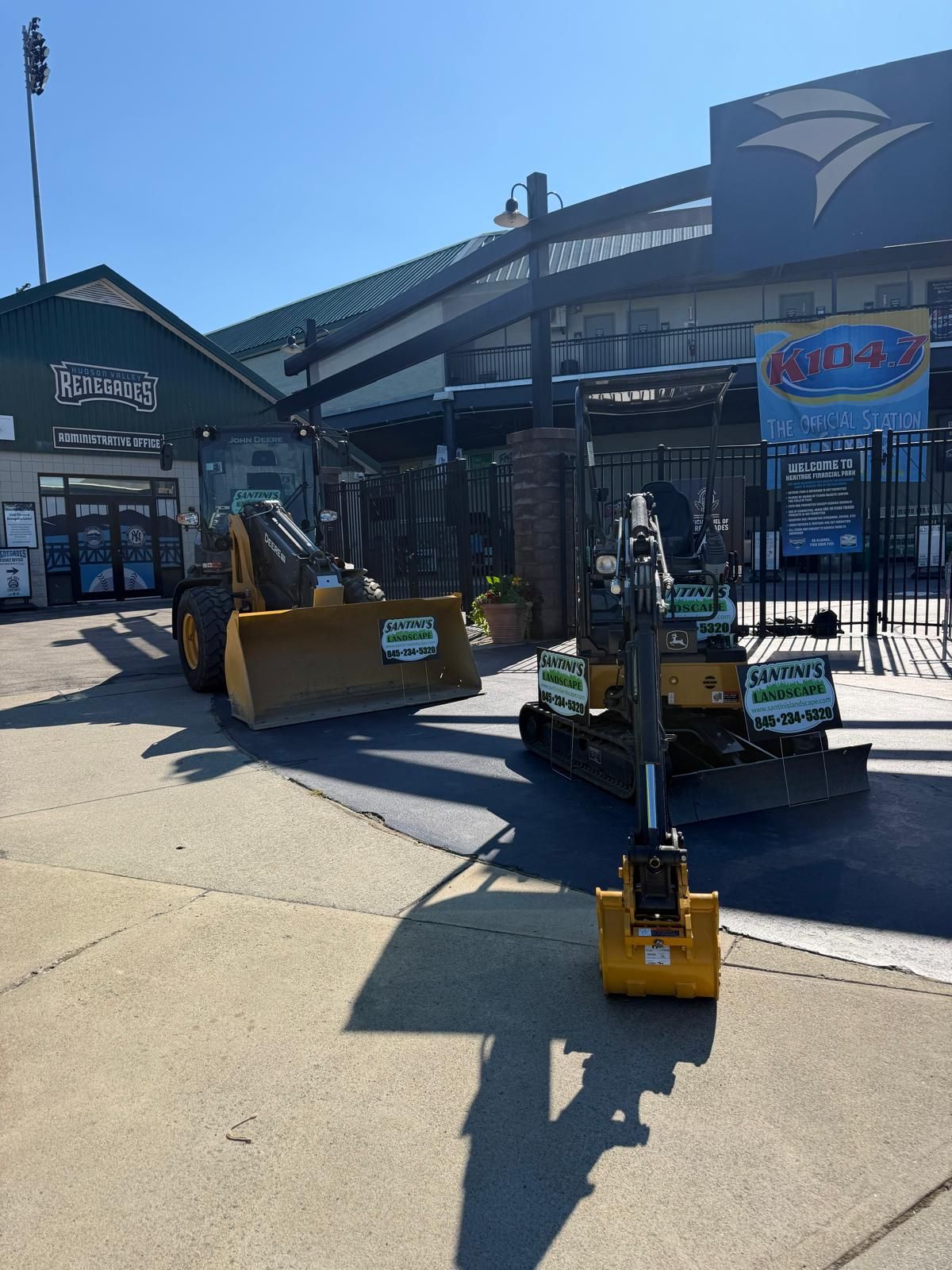 Construction equipment and a small roller in front of a sports stadium entrance on a sunny day