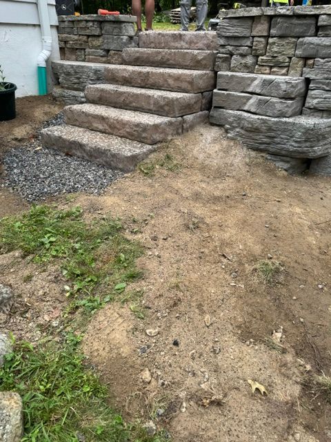 Stone steps and retaining wall in a sloped backyard with patchy dirt and gravel ground