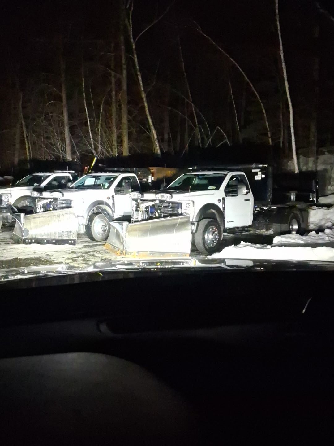Three Santini white pickup trucks parked in a snowy lot at night, lit by headlights.