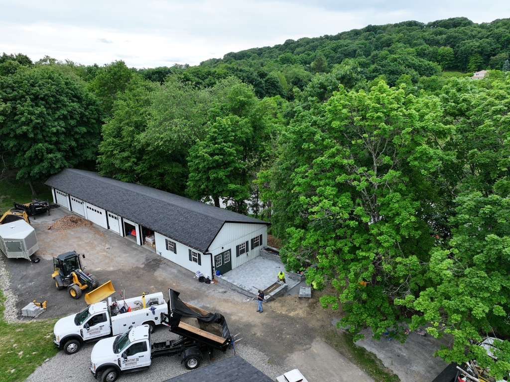 Aerial view of a white worksite building with trucks and equipment beside a wooded hillside
