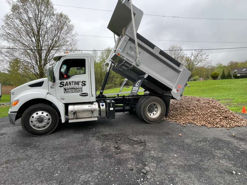 White dump truck unloading a pile of gravel beside a grassy field