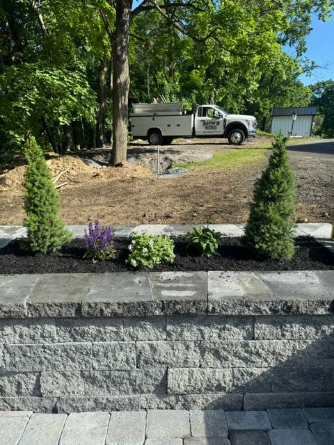 Landscaped front yard with stone wall, flowers, trees, and a parked white truck in the driveway