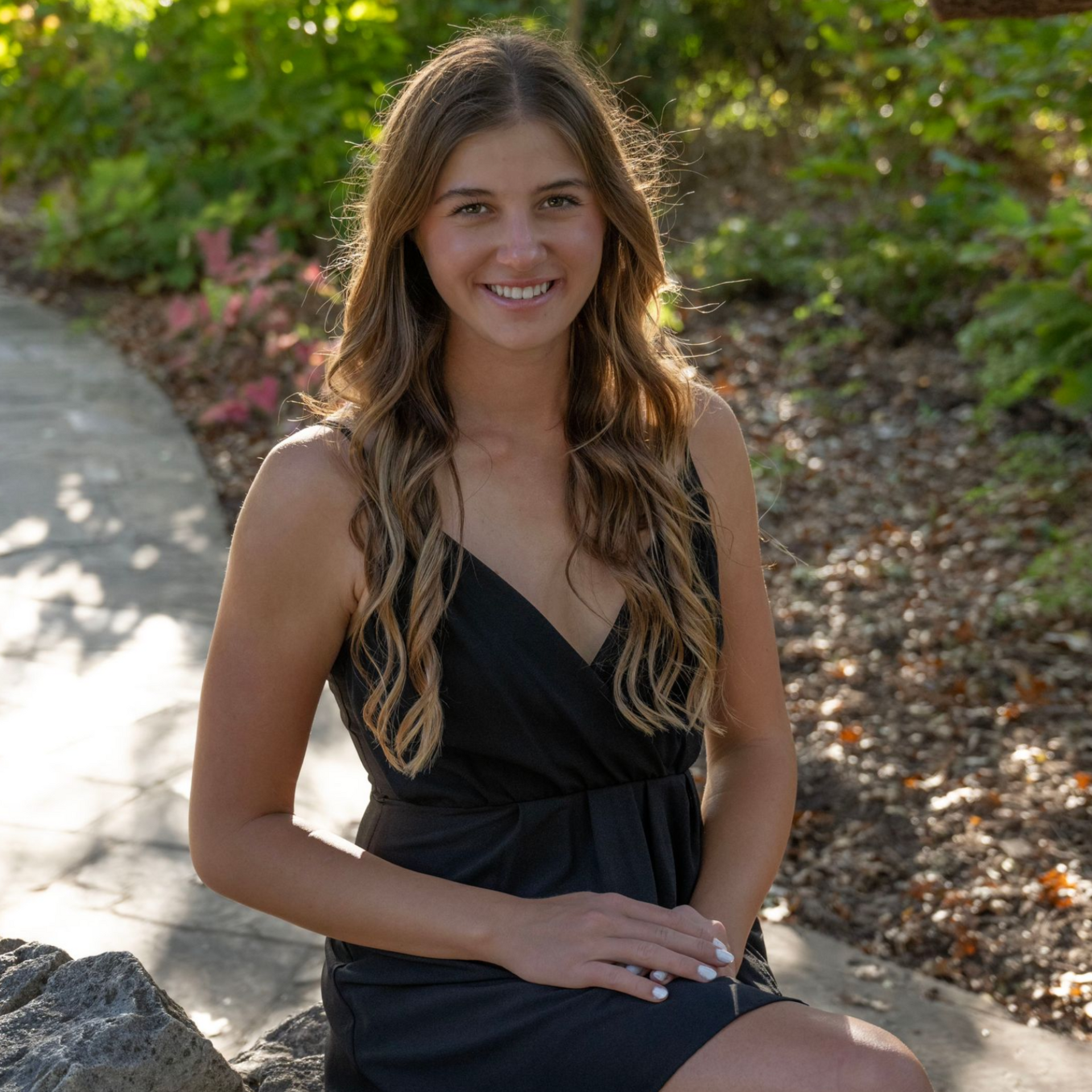 Woman in a black dress smiling on a sunlit garden path