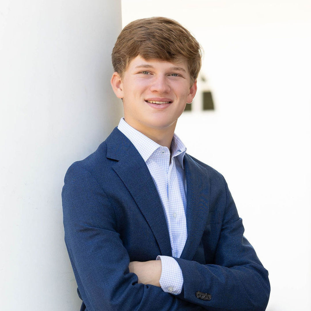 Smiling person in a blue blazer standing with arms crossed against a white wall