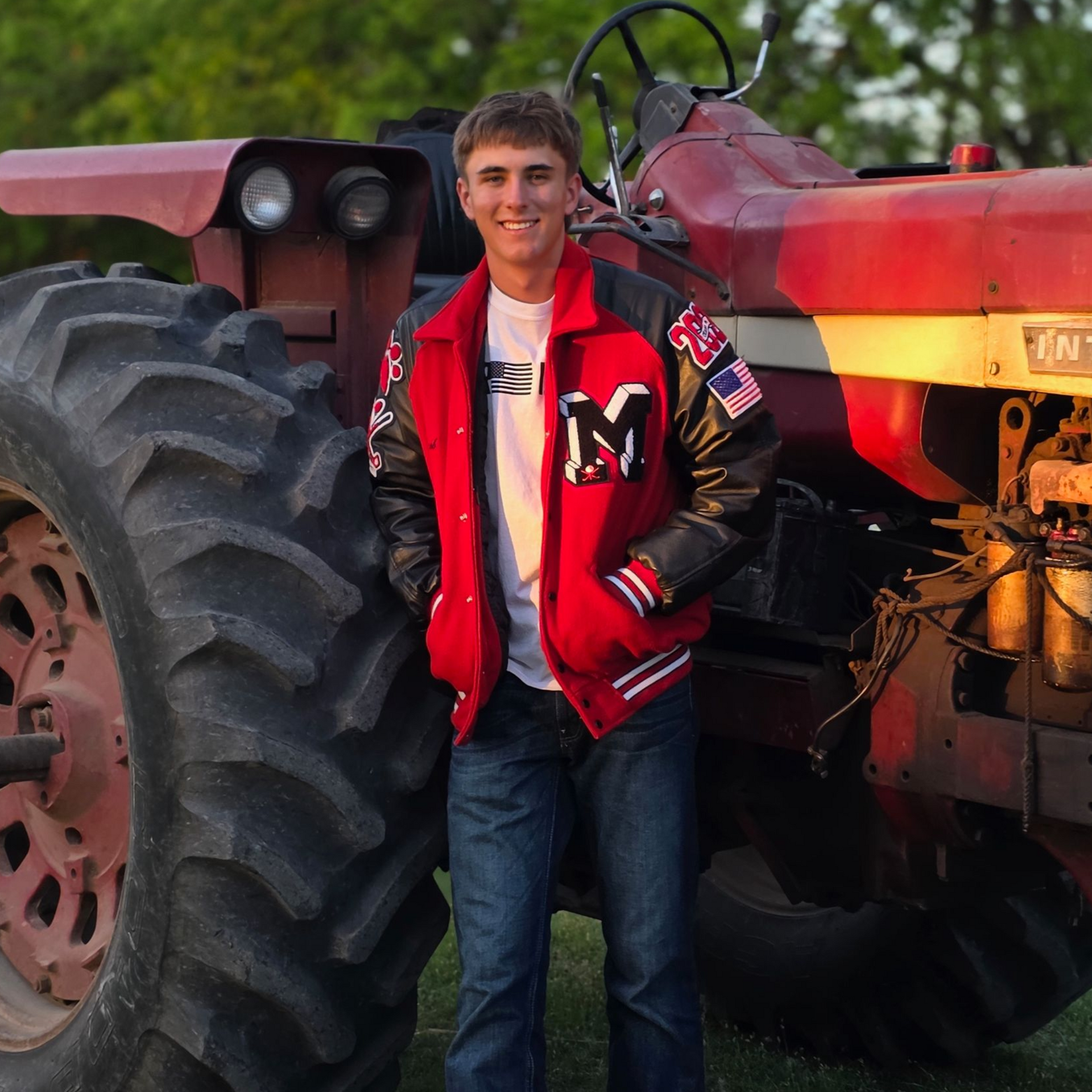 Person in a red jacket leaning against a red tractor outdoors at sunset