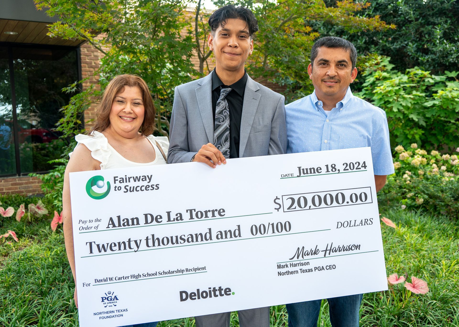 Three people holding a large $20,000 check outdoors with greenery behind them.